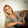 Women with red Cap, blonde Hair, Short grey Shirt sitting in front of a white wall